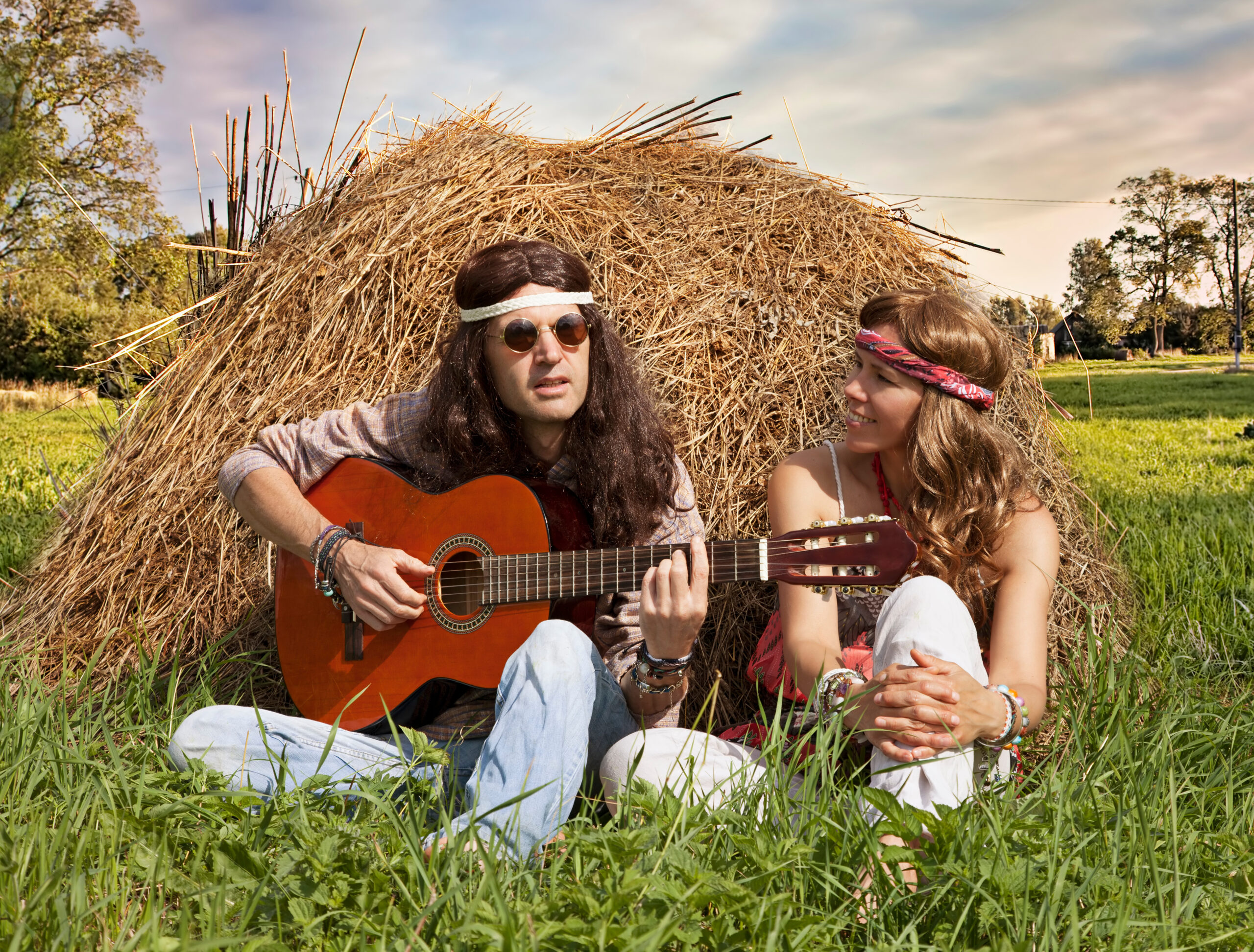 Hippie couple in the 1960s playing guitar on the haystack in the midst of rural meadow