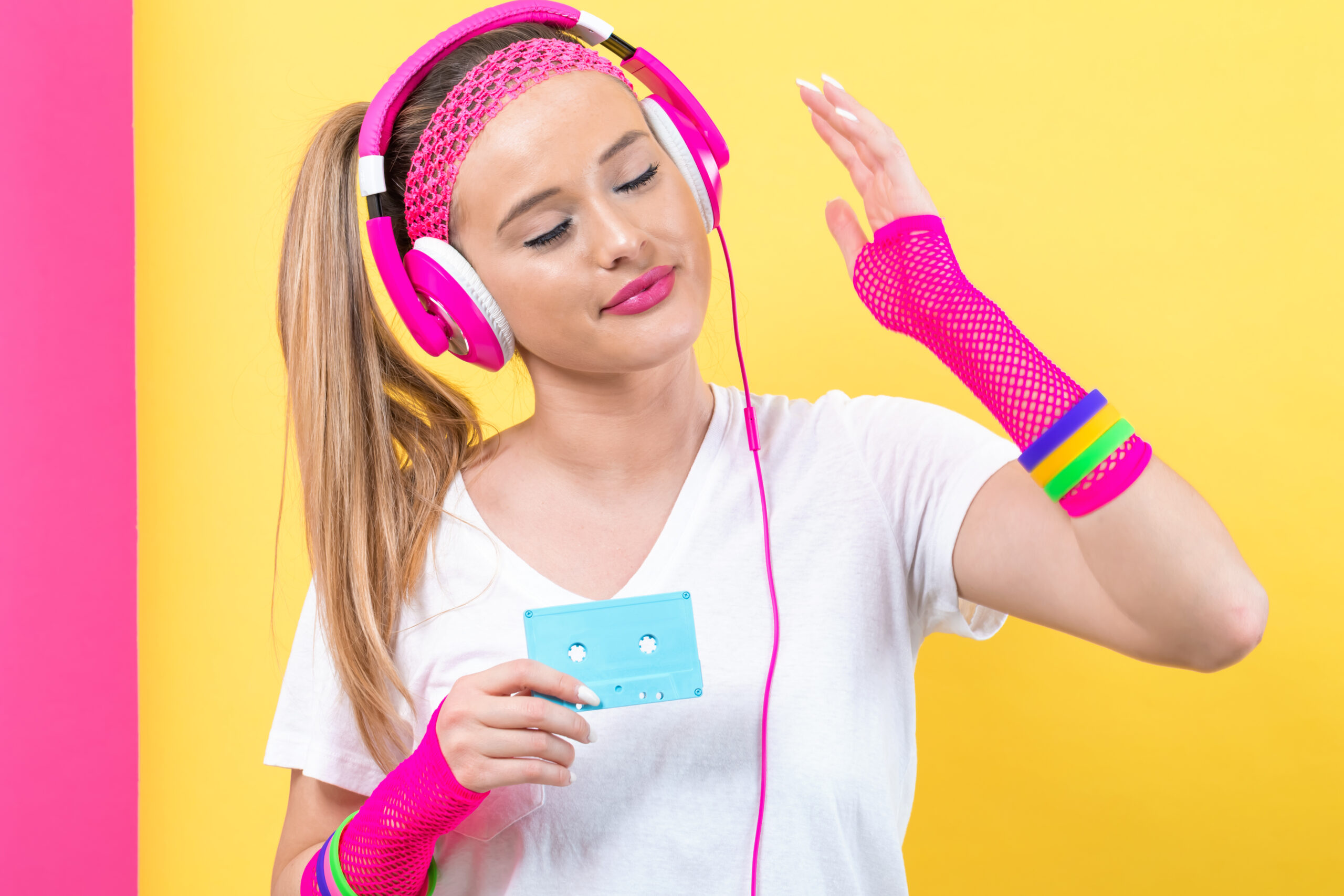 Woman in 1980's fashion holding a cassette tape on a split yellow and pink background